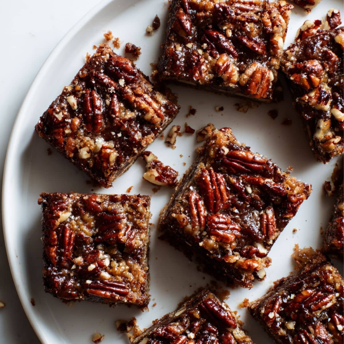 Top-down photo of gooey pecan pie brownies with caramelized pecan topping on a white kitchen table.