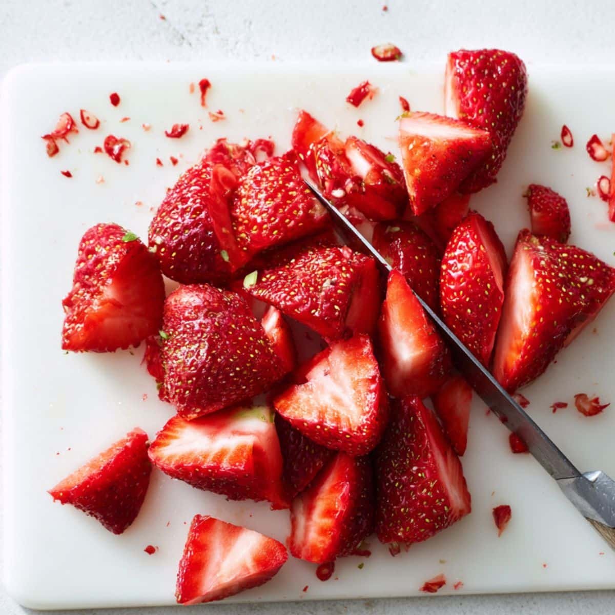 Hulling and slicing fresh strawberries on white cutting board.	