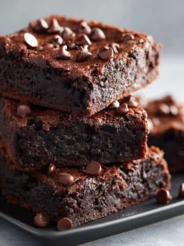 Fudgy homemade protein brownies stacked with chocolate chips on a white kitchen counter