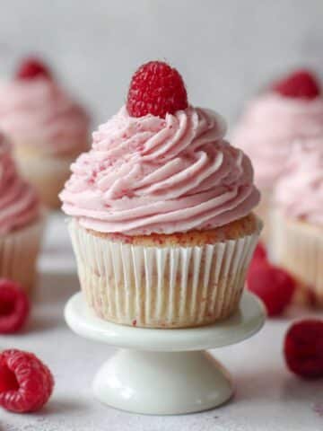 Freshly frosted raspberry cupcake on white stand with a raspberry on top