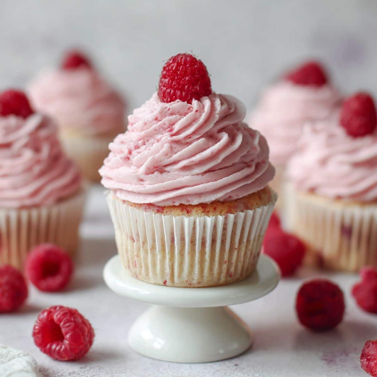 Freshly frosted raspberry cupcakes on white stand with a raspberry on top	