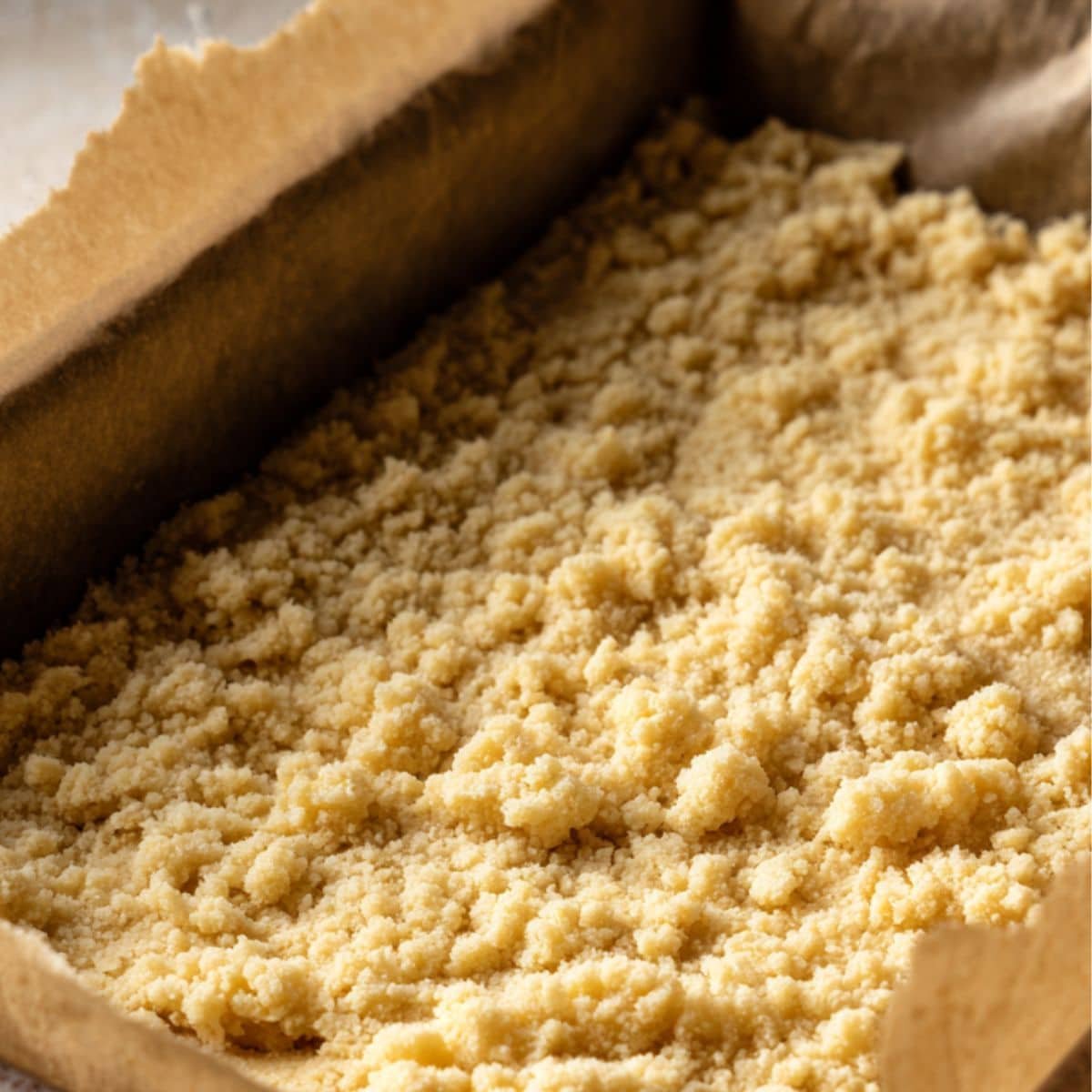 Shortbread crust being pressed into a baking pan	