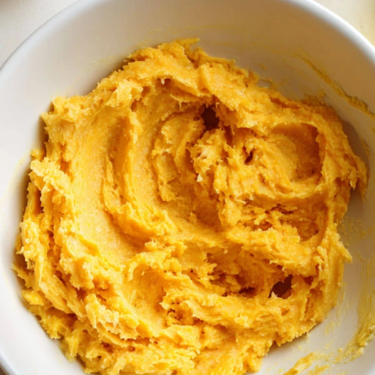 Mixing pumpkin puree and mashed bananas in a bowl on a white counter