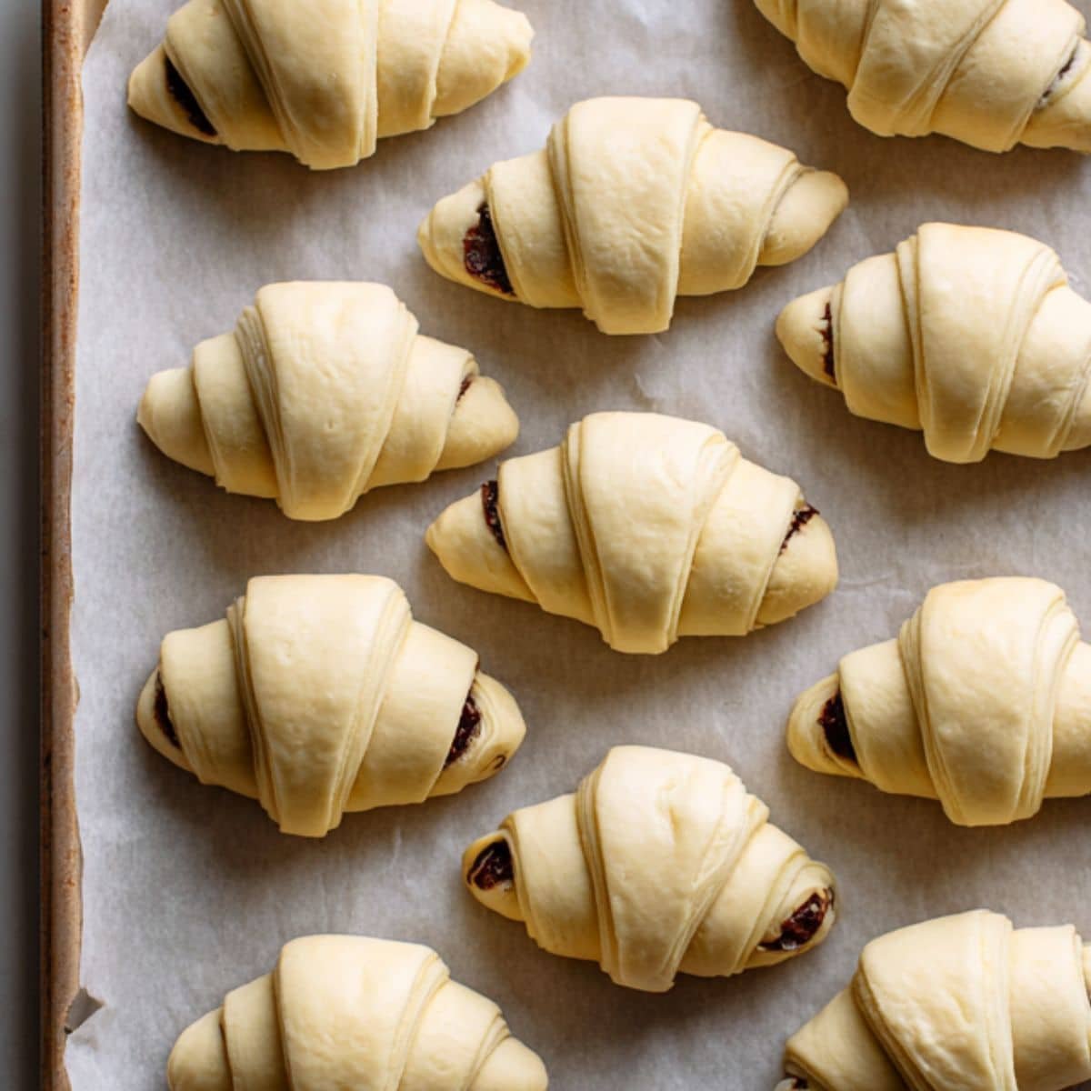 Rolling puff pastry around chocolate batons with egg wash on white counter.