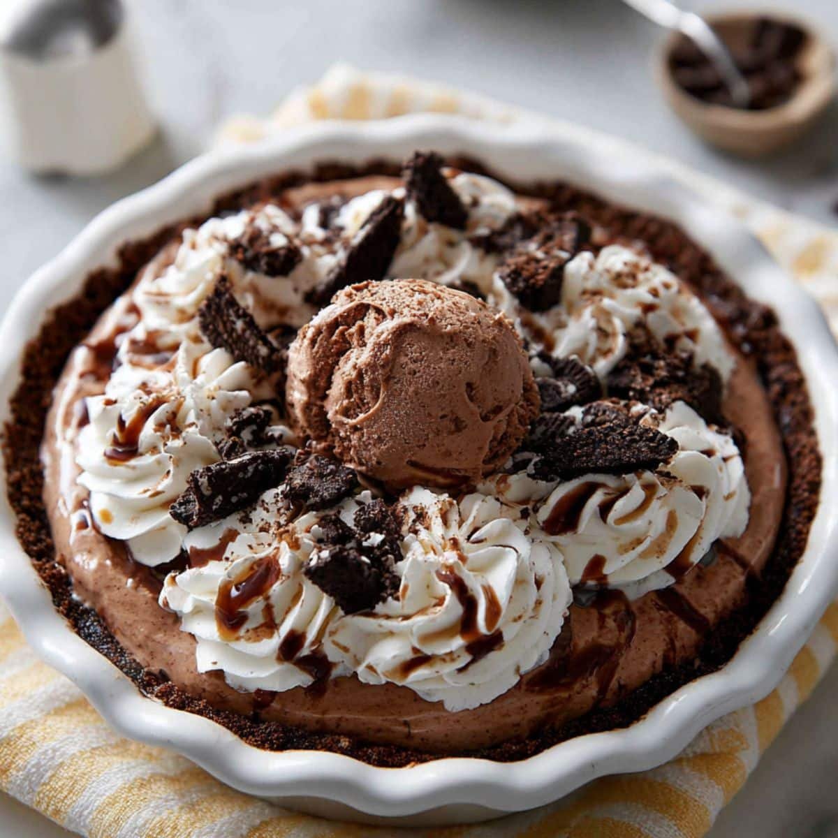 Layering chocolate coffee ice cream, fudge, and toppings in a white pie pan for Mississippi mud pie ice cream	