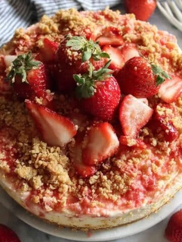 homemade strawberry crunch cheesecake topped with strawberry on a white plate
