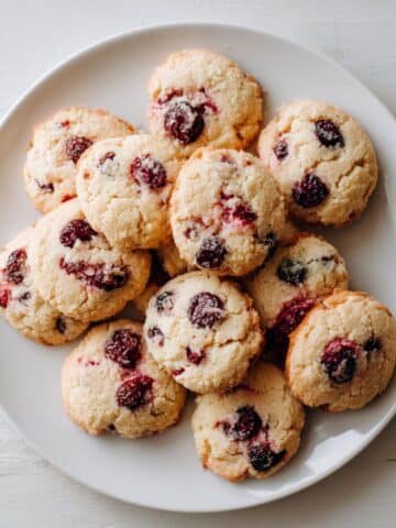 Homemade cherry cookies cooling on parchment paper, photographed from above on a white kitchen table.