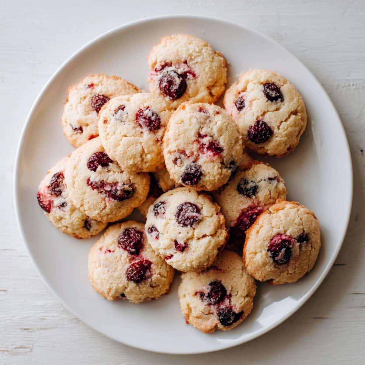 Homemade cherry cookies cooling on parchment paper, photographed from above on a white kitchen table.