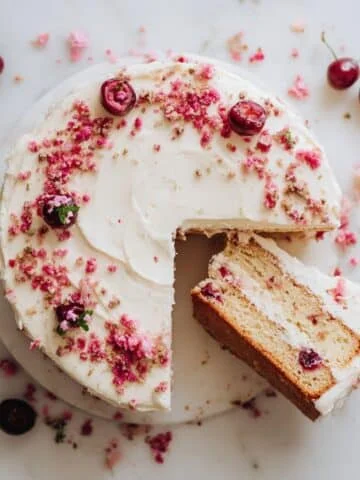 Homemade cherry chip cake with cream cheese frosting, sliced on a white kitchen table, top-down view.