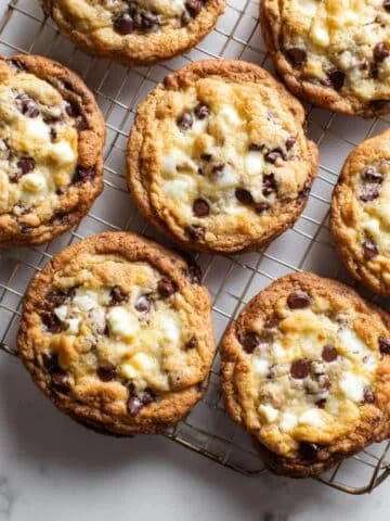 Golden brown chocolate chip cheesecake cookies with creamy filling cooling on a wire rack in a white kitchen, homemade and chewy