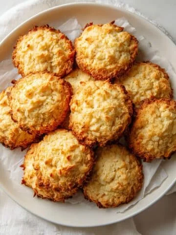 Top-down shot of golden brown coconut cookies on parchment-lined baking tray in a bright white kitchen, homemade look