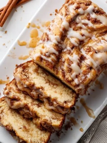 Top-down sliced apple fritter bread with glaze and crumbs on a white kitchen table.