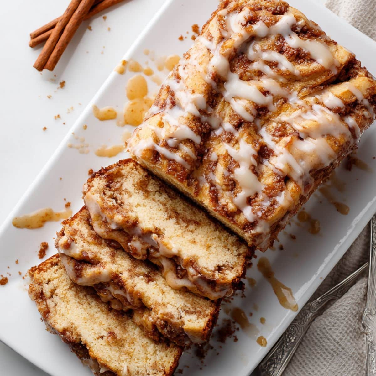 Top-down sliced apple fritter bread with glaze and crumbs on a white kitchen table.