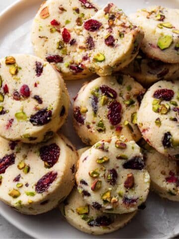 Top-down homemade photo of cranberry pistachio shortbread cookies on parchment paper, rustic and imperfect, taken on a white kitchen table.