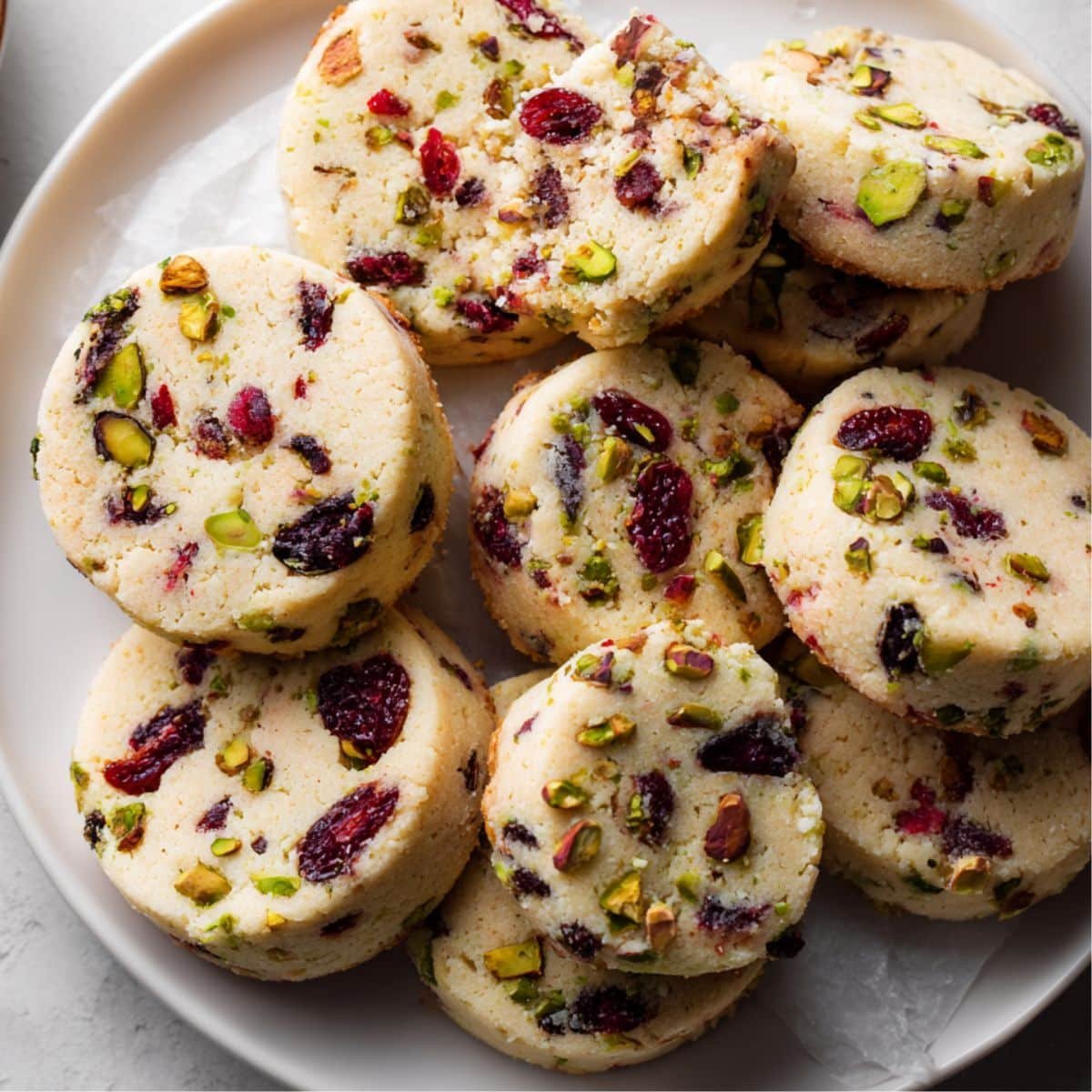 Top-down homemade photo of cranberry pistachio shortbread cookies on parchment paper, rustic and imperfect, taken on a white kitchen table.