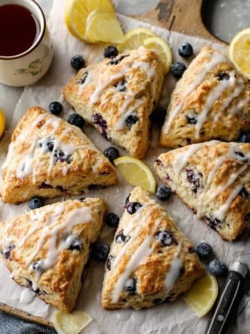 Overhead photo of eight lemon blueberry scones on parchment over a white kitchen table with a light glaze.