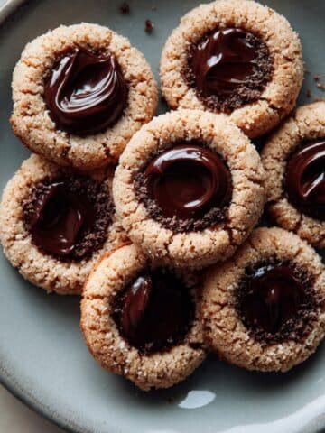 Top-down tray of thumbprint cookies chocolate with ganache on a white table.