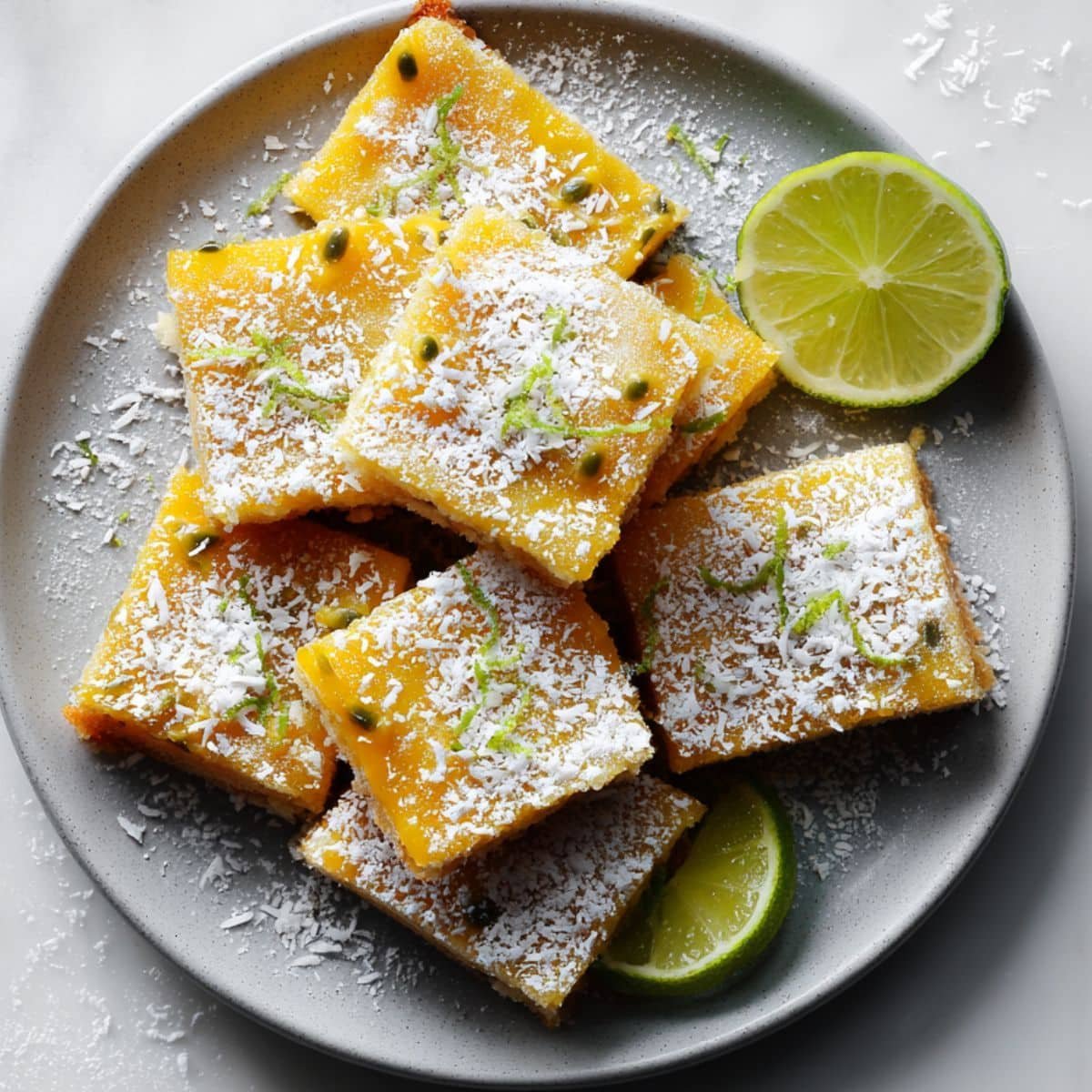 Homemade passionfruit bars cut into squares on a white kitchen table, dusted with powdered sugar and topped with coconut flakes and lime zest.