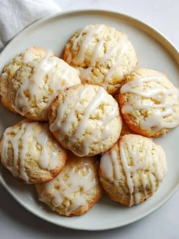 Freshly baked ricotta cookies recipe with glaze cooling on a wire rack on a white kitchen table.