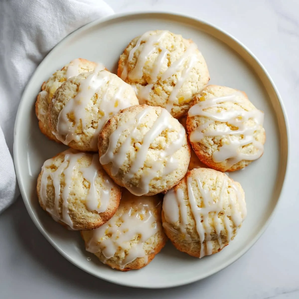 Freshly baked ricotta cookies recipe with glaze cooling on a wire rack on a white kitchen table.