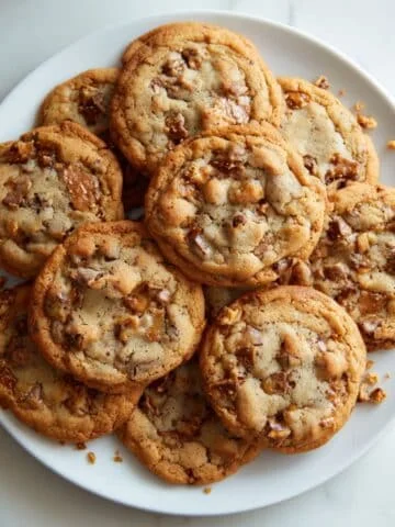 Top-down view of homemade toffee cookies with chocolate chips and toffee bits on a white kitchen table.