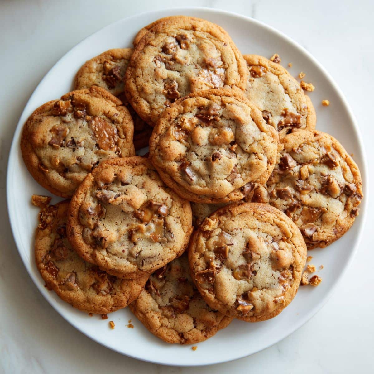 Top-down view of homemade toffee cookies with chocolate chips and toffee bits on a white kitchen table.