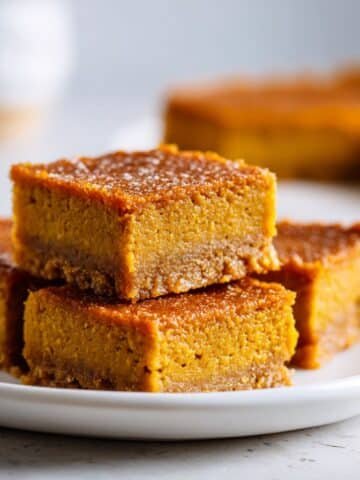 Homemade vegan pumpkin pie bars cut into squares on a white kitchen table with parchment paper, shot from above.
