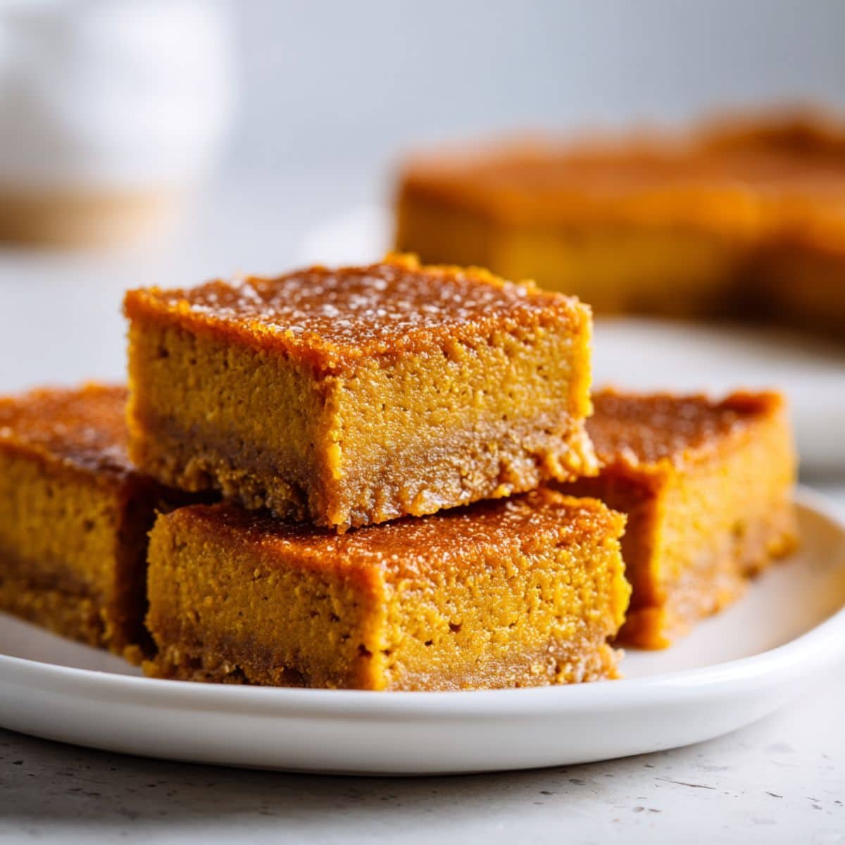 Homemade vegan pumpkin pie bars cut into squares on a white kitchen table with parchment paper, shot from above.