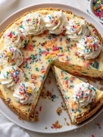 Homemade funfetti cheesecake with rainbow sprinkles and graham cracker crust on a white kitchen table, top-down shot.