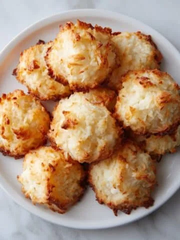Homemade gluten free coconut macaroons cooling on parchment paper, photographed from above on a white kitchen counter.
