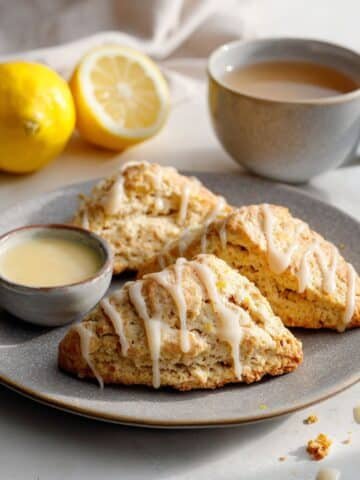 homemade lemon scones recipe on plate with light glaze and crumbs on a white kitchen table.
