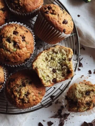 Top-down photo of chocolate chip zucchini muffins on a white table, one torn open, crumbs and a few chips around.