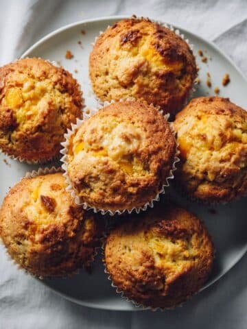 Freshly baked peach muffins on a white kitchen table, homemade and imperfect, top-down shot.