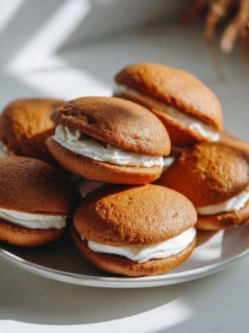 Homemade pumpkin whoopie pies with cream cheese filling on a white kitchen table, shot from above