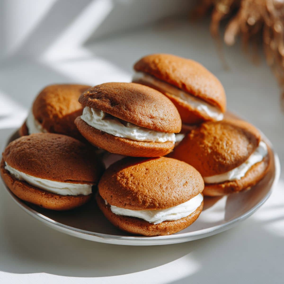 Homemade pumpkin whoopie pies with cream cheese filling on a white kitchen table, shot from above