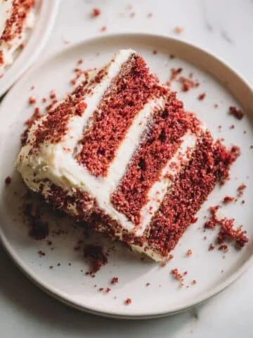 Homemade red and white cake with cream cheese frosting, sliced to reveal vibrant red layers, on a white kitchen table, photographed from above