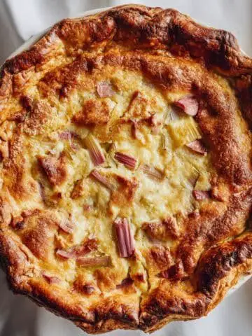 Homemade rhubarb custard pie on a white kitchen table, rustic crust with creamy custard and rhubarb filling, top-down shot.