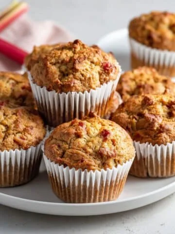 Homemade rhubarb muffins recipe cooling on a white kitchen table in paper liners, golden brown and rustic.