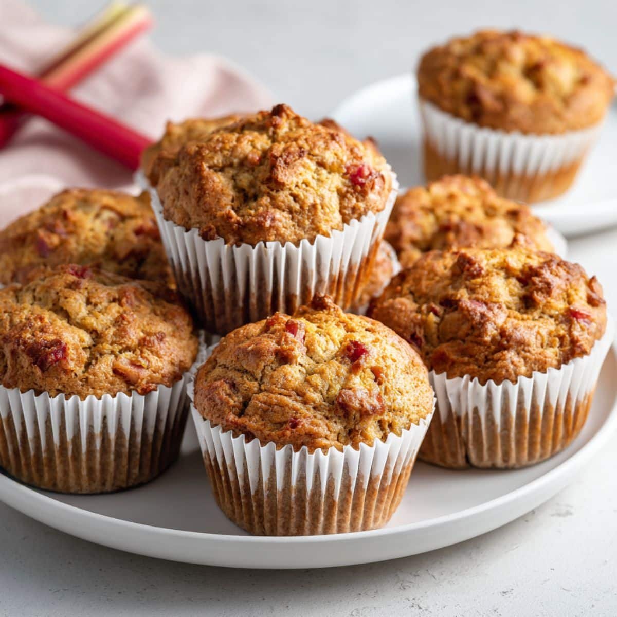 Homemade rhubarb muffins recipe cooling on a white kitchen table in paper liners, golden brown and rustic.