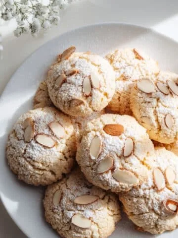 Homemade almond cookies recipes on a white table, top-down view with sliced almonds and powdered sugar.