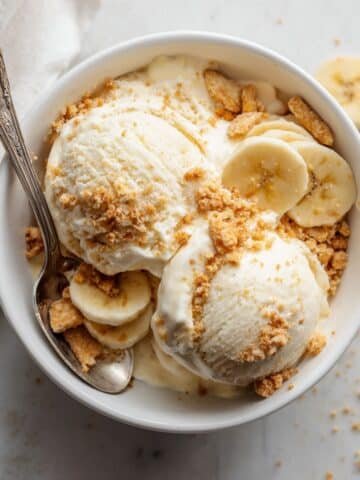 Homemade banana pudding ice cream in a white bowl topped with vanilla wafers and banana slices on a white kitchen counter