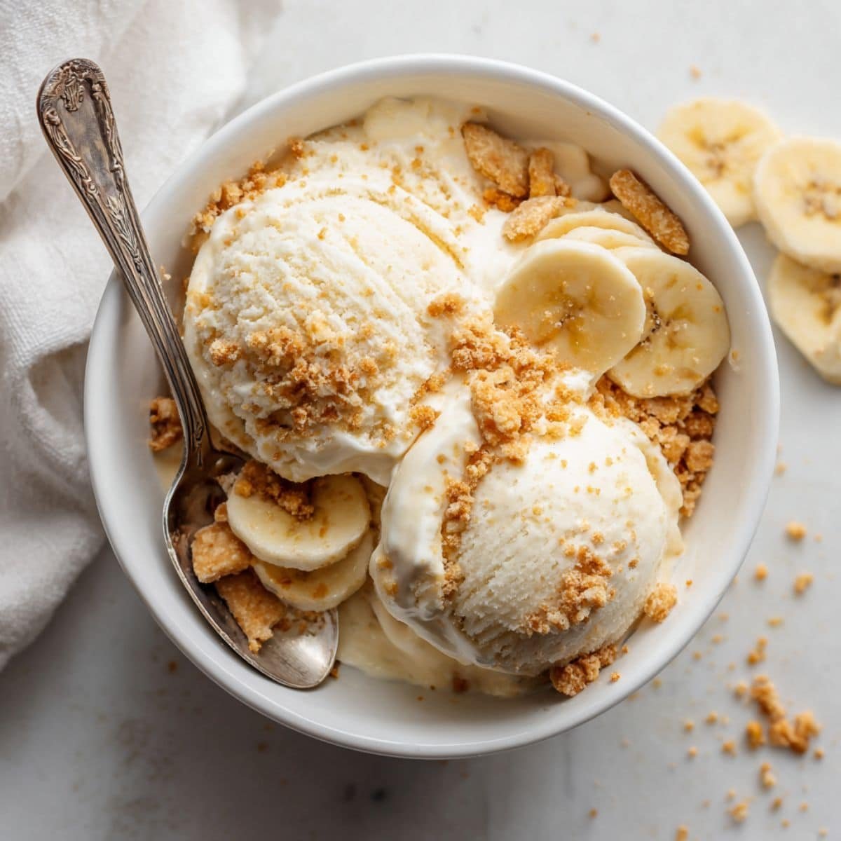 Homemade banana pudding ice cream in a white bowl topped with vanilla wafers and banana slices on a white kitchen counter