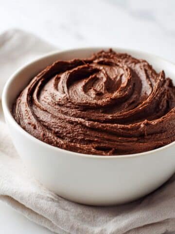 Bowl of creamy homemade chocolate fudge frosting on a white kitchen counter