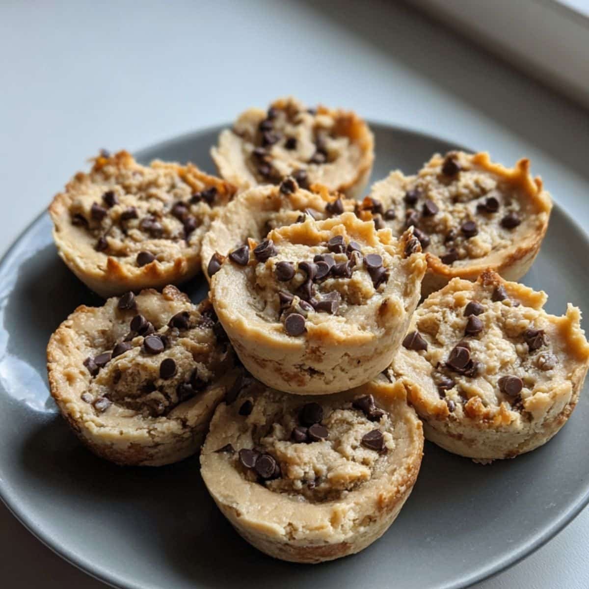 Homemade cookie dough cups on a white kitchen table, rustic and imperfect with chocolate chips and peanut butter filling, shot from above