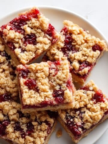 Homemade cranberry bars cut into squares on a white kitchen table, with crumbs scattered around, shot from above