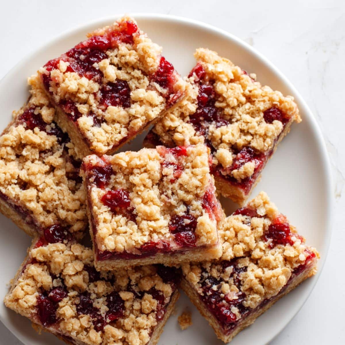 Homemade cranberry bars cut into squares on a white kitchen table, with crumbs scattered around, shot from above