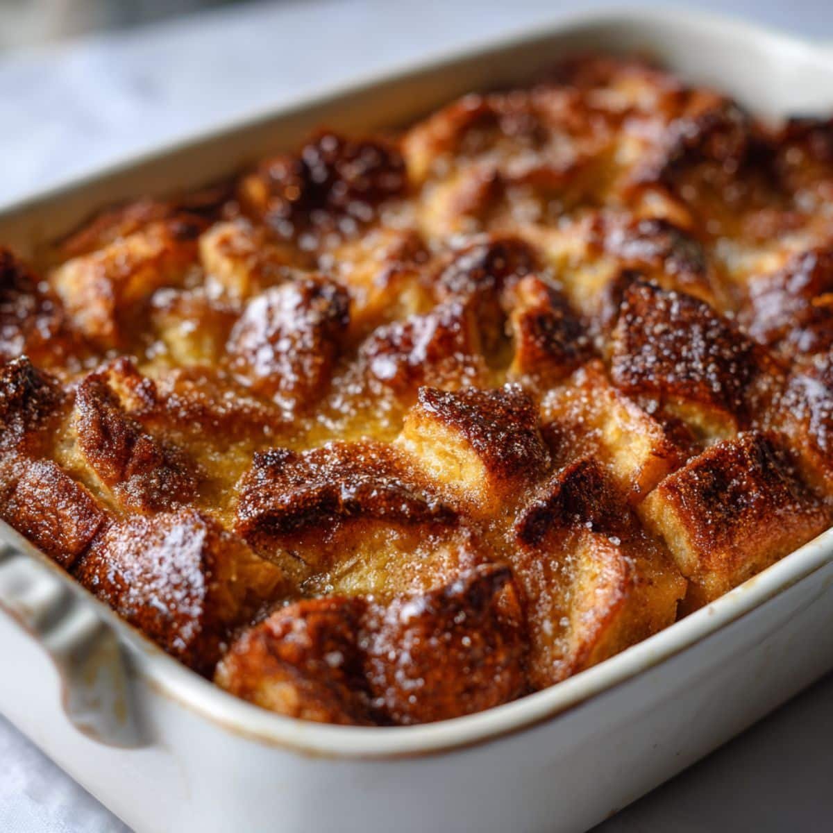Freshly baked homemade croissant bread pudding recipe in a white baking dish, golden and caramelized on a white kitchen table