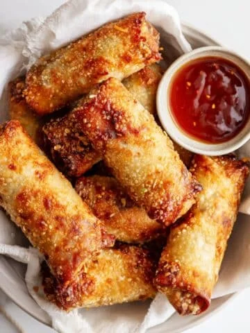 Crispy golden egg roll air fryer recipe served on a white plate with dipping sauce in a bright white kitchen