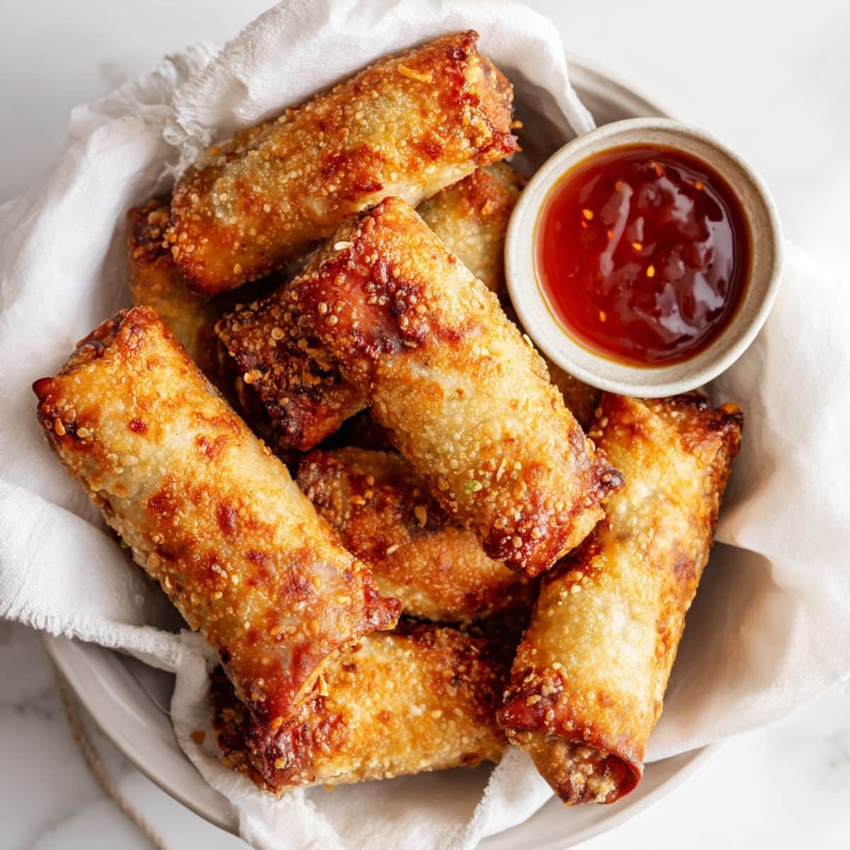 Crispy golden egg roll air fryer recipe served on a white plate with dipping sauce in a bright white kitchen