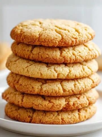Top-down view of chewy brown butter sugar cookies stacked on a white plate in a white kitchen